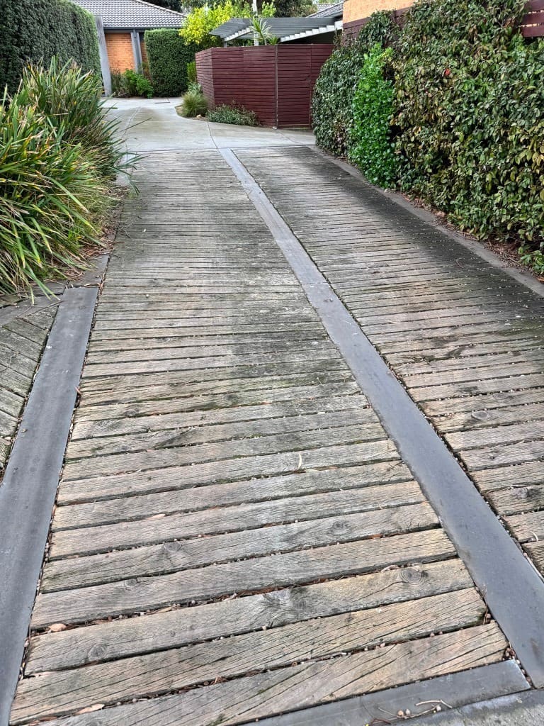 The timber bridge deck in July 2026, weathered grey but flat and intact, running towards the garage.