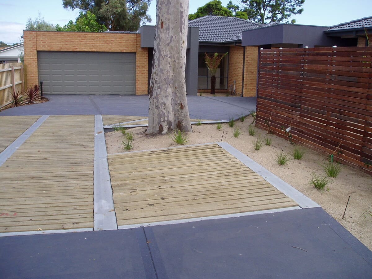 The finished driveway in February 2006: timber deck panels, a sand bed with new planting around the trunk, and coloured concrete beyond.